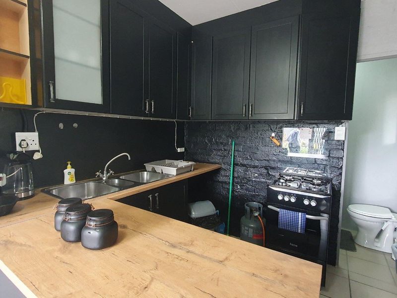 Compact kitchen featuring black cabinetry, wooden countertops, a gas stove, and an exposed brick wall, with an adjacent bathroom visible.