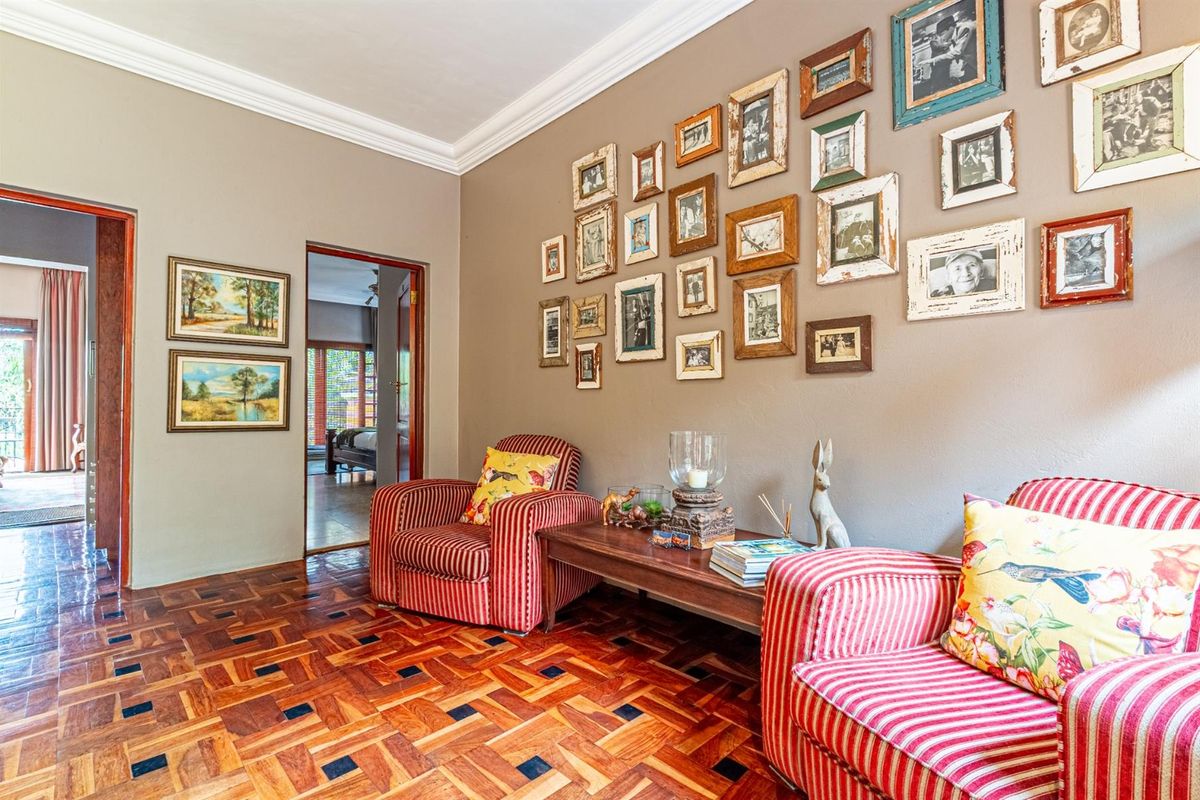 A cozy living room featuring traditional parquet flooring, crown molding, and a gallery wall, with direct access to adjacent rooms.