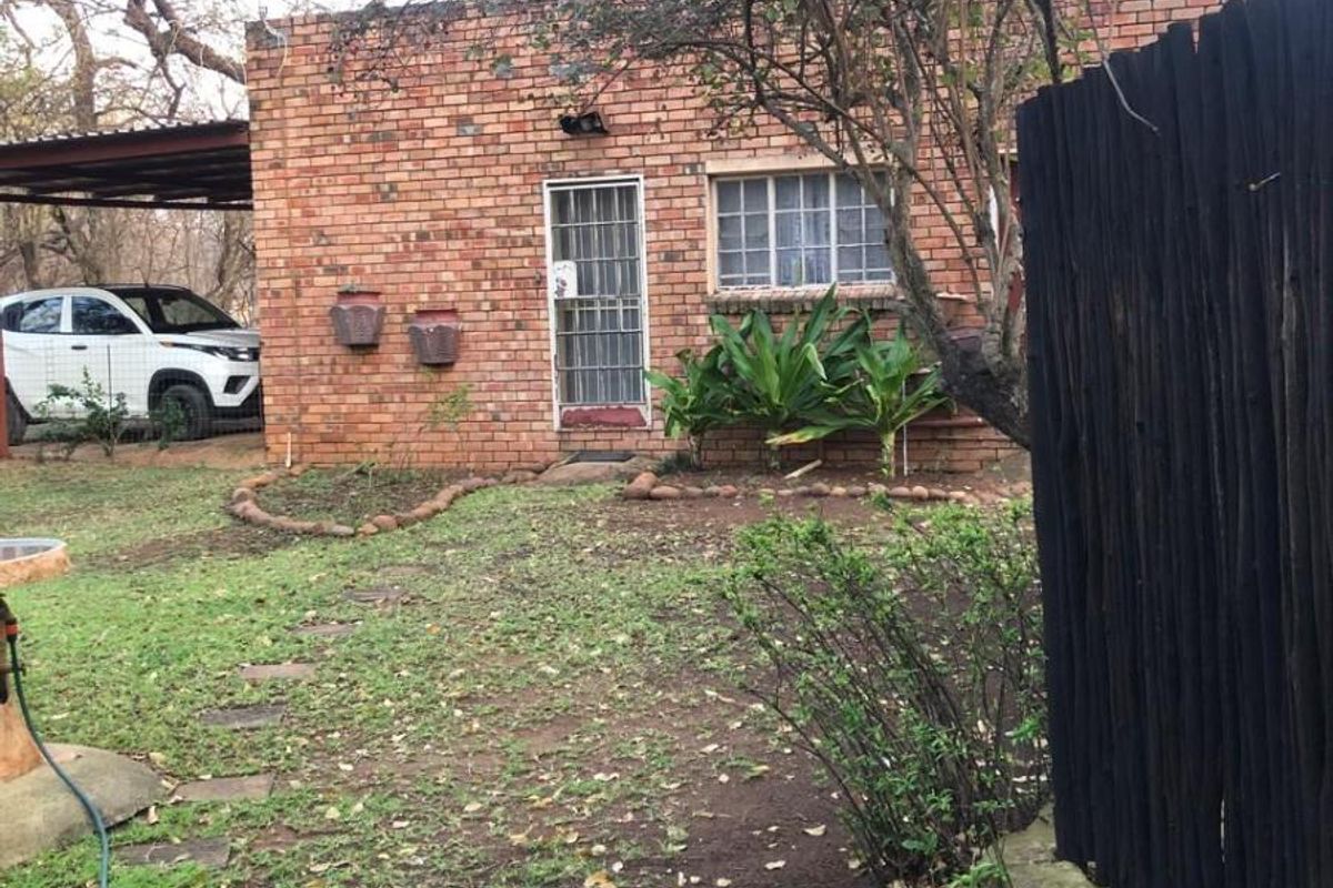 Rear view of a face brick house featuring a small garden, attached carport, and timber fencing.