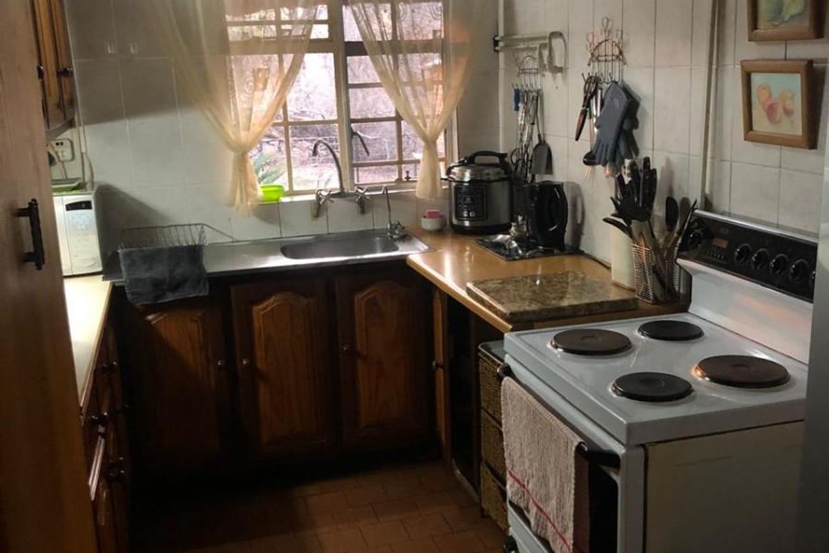 A compact, dated kitchen featuring wooden cabinetry, tiled backsplash, and a freestanding electric stove under an exposed beam ceiling.