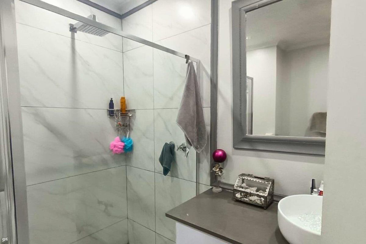 Modern bathroom featuring a walk-in shower with marble-look wall tiles, a vanity with a vessel sink, and a framed wall mirror.