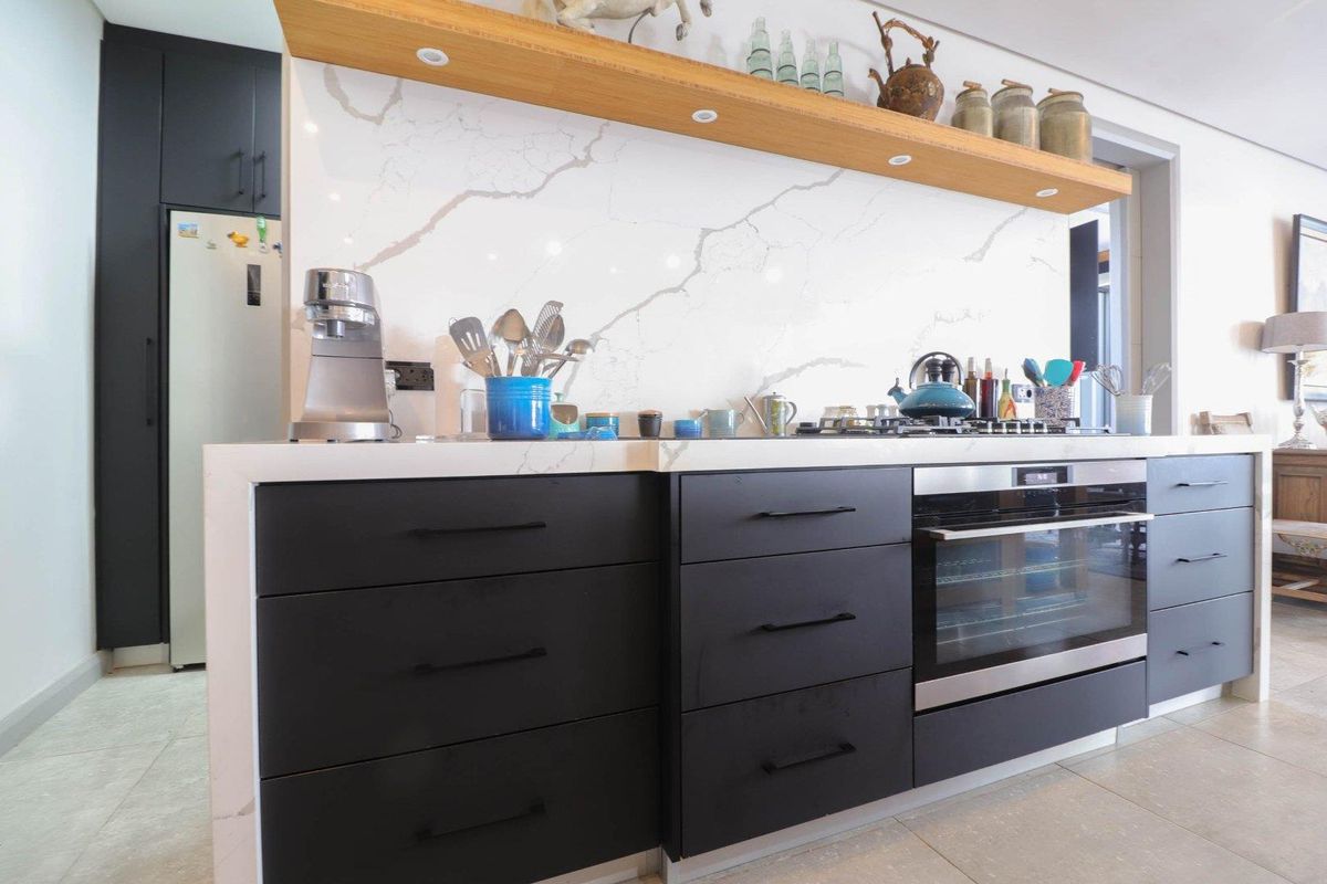 Modern kitchen featuring matte black cabinetry, a marble-look stone countertop and backsplash, integrated oven, and a floating timber shelf with recessed lighting.