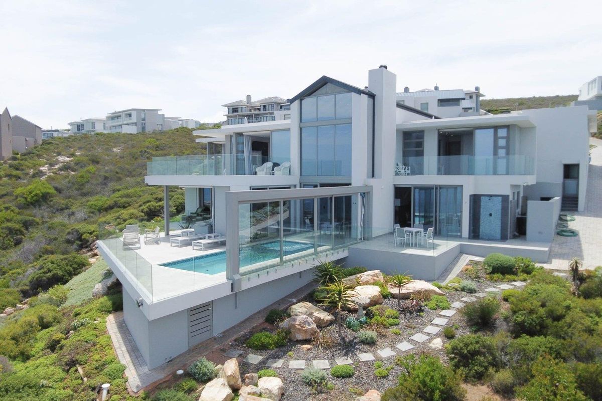 Modern multi-level architectural home featuring expansive glass facades, a cantilevered swimming pool, and spacious balconies overlooking the surrounding landscape.