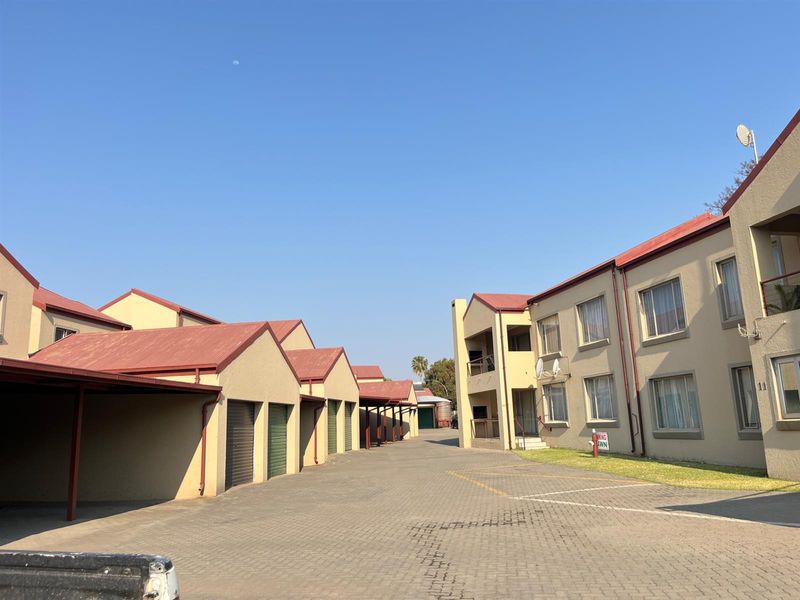Exterior view of an apartment complex featuring a paved driveway, covered parking carports, and multi-story residential units with metal roofing.