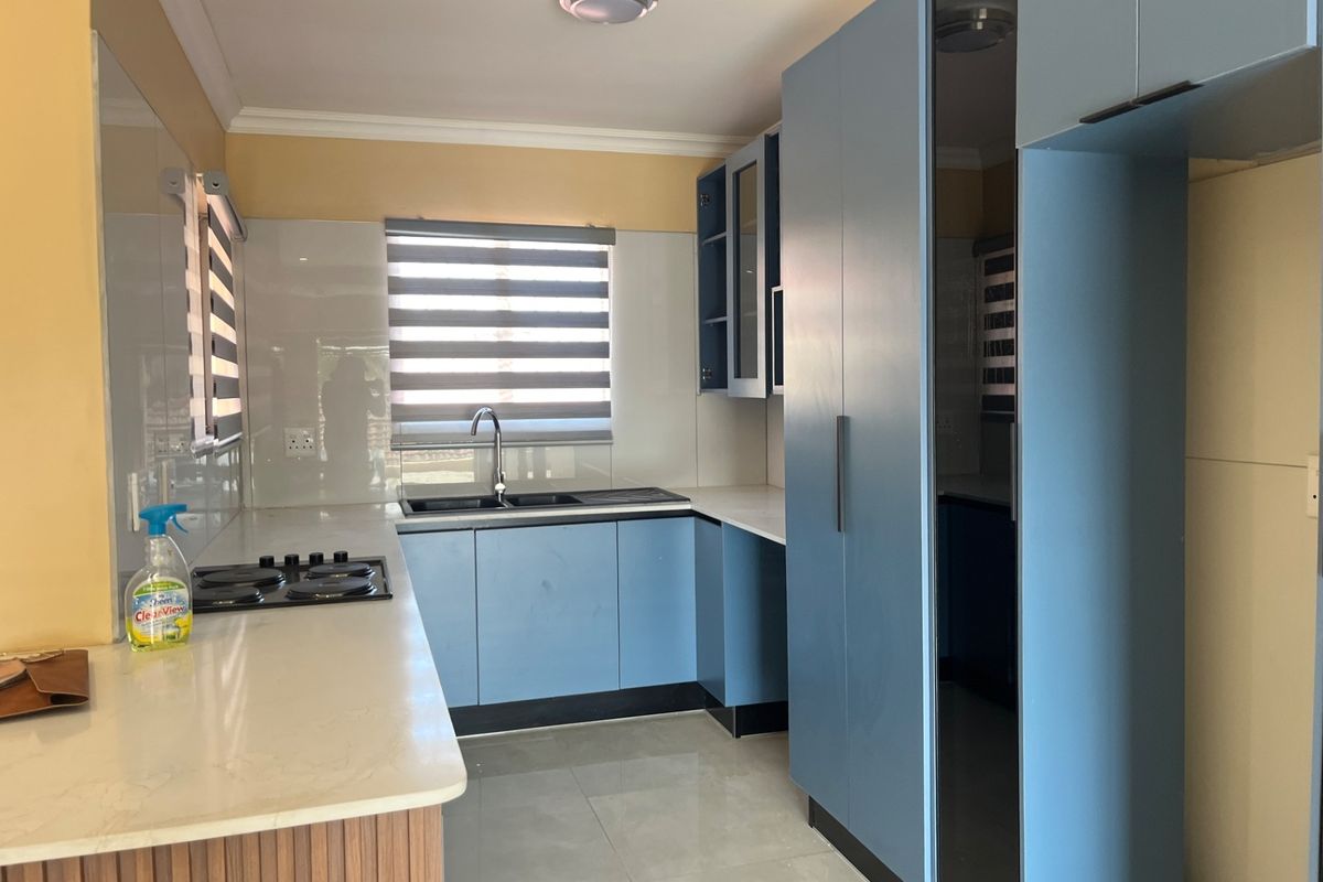 A modern kitchen featuring blue built-in cabinetry, stone countertops, a double sink, and a built-in hob with neutral tiled flooring.