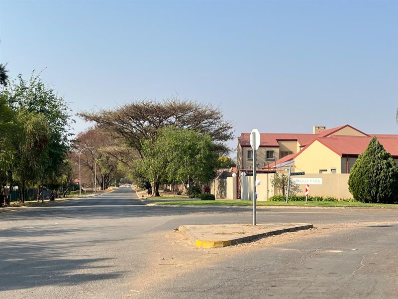 A street view showing the approach to the residential complex with perimeter walls and mature trees.