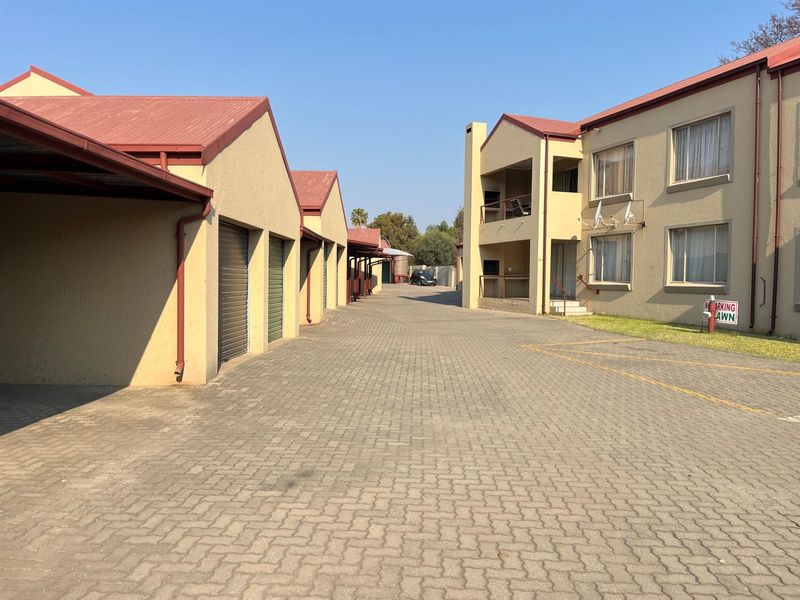 Exterior view of an apartment complex featuring a paved driveway, covered parking carports, and multi-story residential units with balconies.