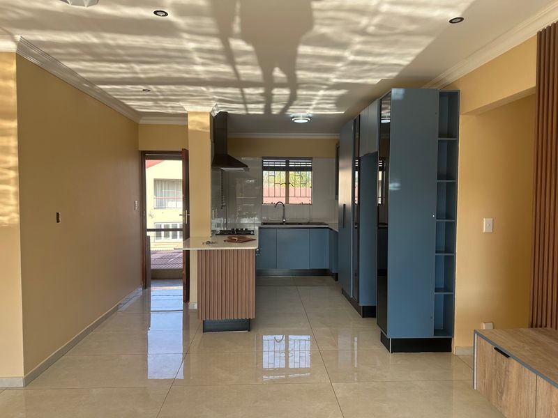 Modern open-plan kitchen featuring blue cabinetry, a central island, and tiled flooring, leading to an outdoor balcony area.