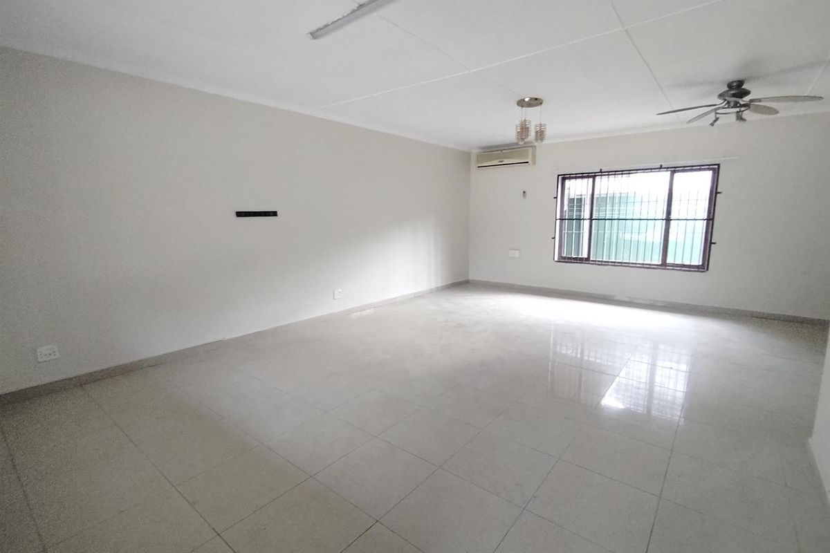 A spacious, empty living room featuring tiled flooring, a ceiling fan, and a wall-mounted air conditioning unit.