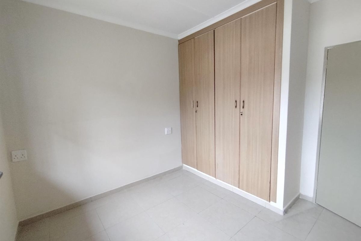 A clean, neutral bedroom featuring light-toned tiled flooring and built-in wooden cupboards.