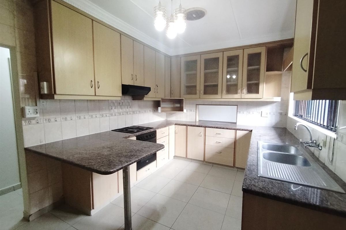 A functional kitchen featuring laminate cabinetry, granite countertops, a built-in oven and hob, and a double stainless steel sink with tiled flooring.