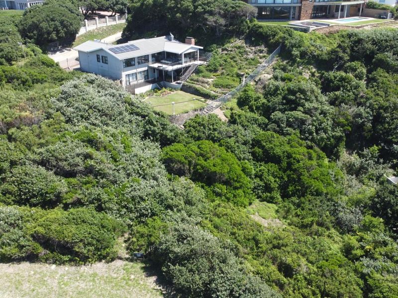 Aerial view of a residential property nestled within dense coastal vegetation, featuring a multi-level home with solar panels and a landscaped garden area.