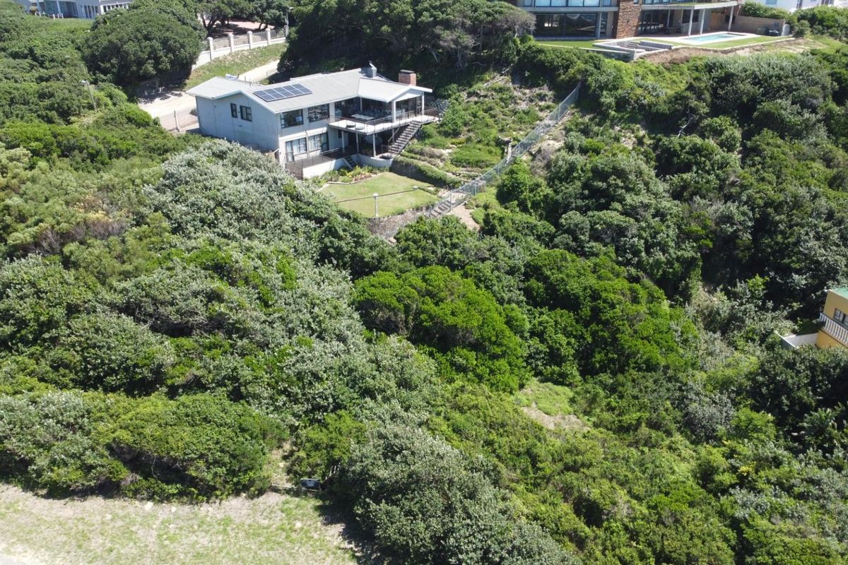 Aerial view of a residential property nestled within dense coastal vegetation, featuring a multi-level home with solar panels and a landscaped garden area.