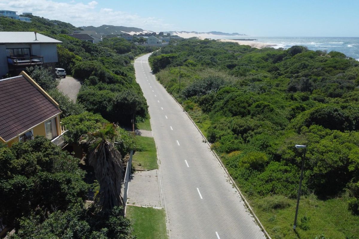 Aerial view of a coastal residential street featuring paved road infrastructure, surrounding lush vegetation, and proximity to the ocean coastline.