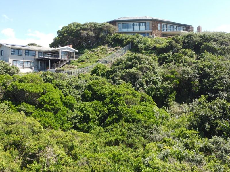 Elevated view of residential properties nestled within a lush, densely vegetated coastal landscape, featuring multi-level structures and outdoor staircases.