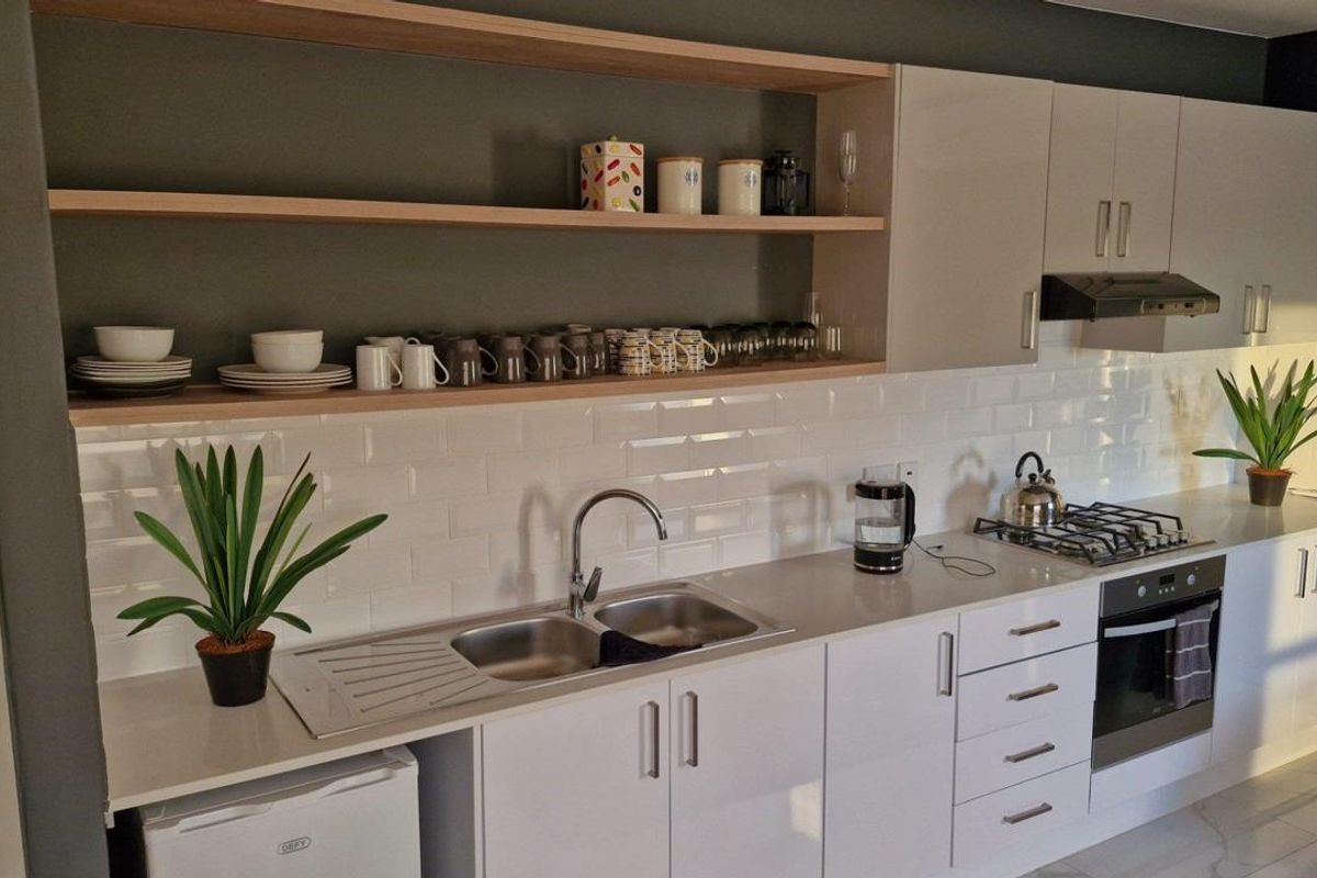 Modern kitchen featuring white cabinetry, subway tile backsplash, integrated oven, gas hob, extractor fan, and a double stainless steel sink with stone countertops.