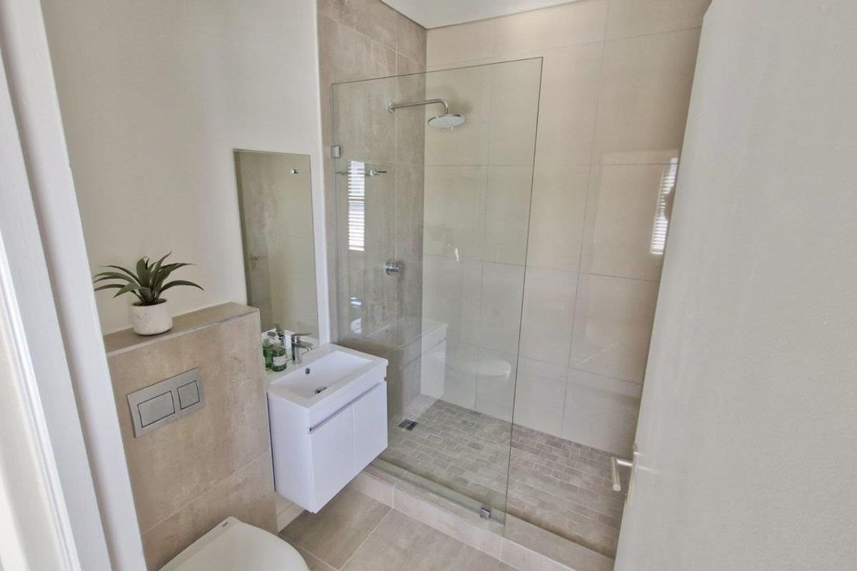 Modern bathroom featuring a walk-in glass shower with neutral wall tiles, a wall-mounted vanity, and a concealed cistern toilet.