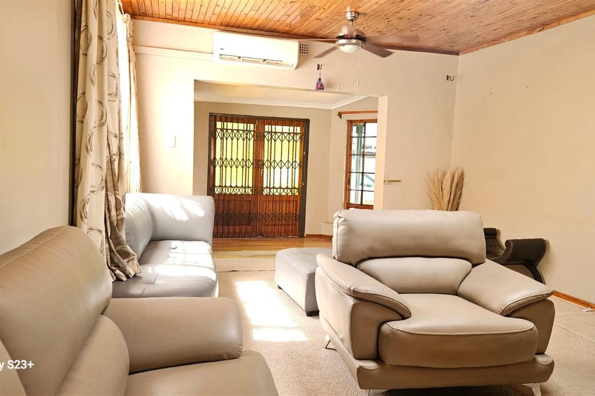 A living room featuring a timber-paneled ceiling, ceiling fan, split-system air conditioning, and a security gate leading to the exterior.