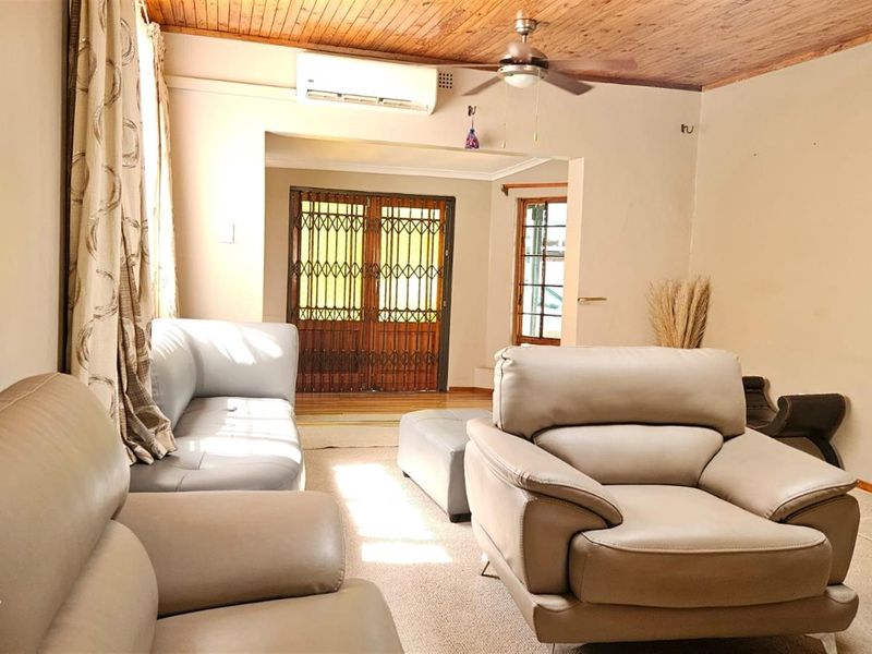 A living room featuring a timber-paneled ceiling, ceiling fan, split-system air conditioning, and a security gate leading to the exterior.