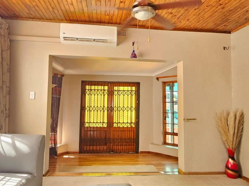 Living area featuring a timber ceiling, ceiling fan, split-system air conditioning, and a secure entrance with timber-framed windows and flooring.