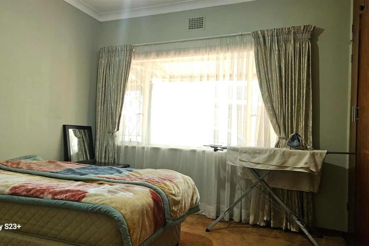 A standard bedroom featuring a built-in wardrobe and large window with curtains, providing natural light and functional storage space.