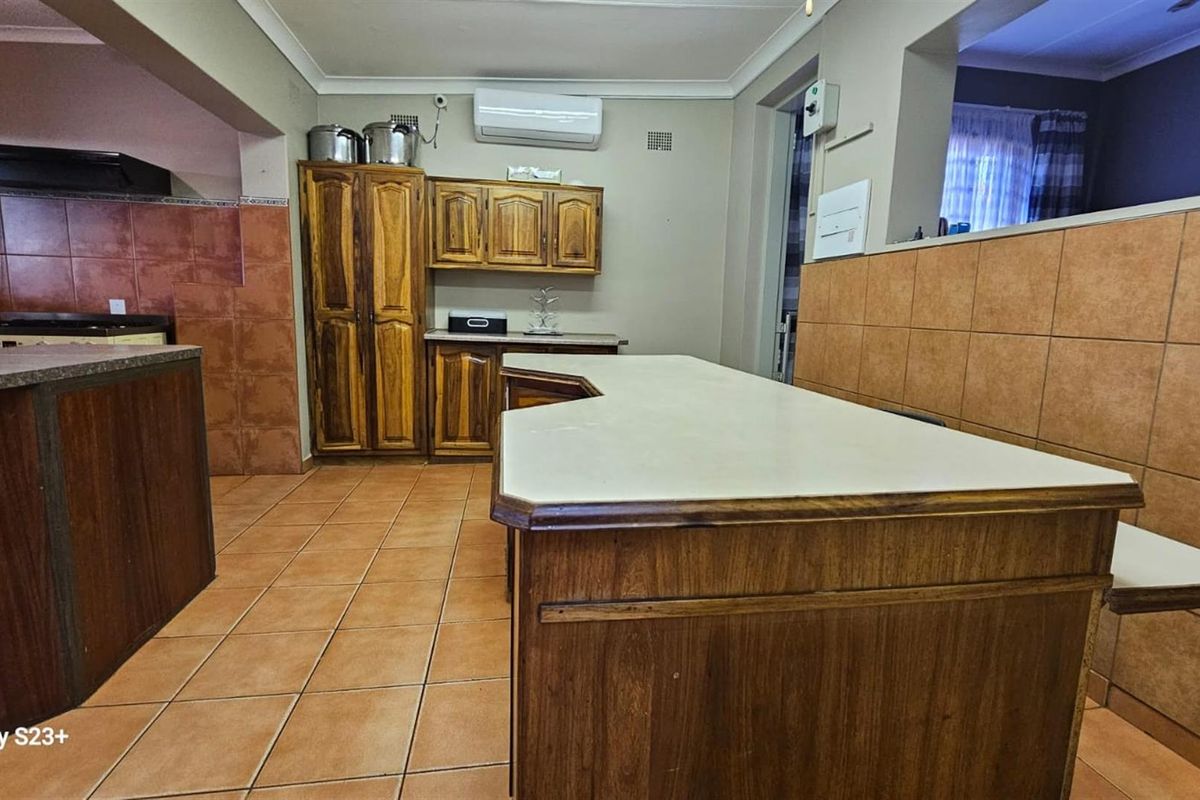 A functional kitchen featuring wooden cabinetry, tiled flooring, and a central breakfast bar, offering a practical layout with potential for modern updates.