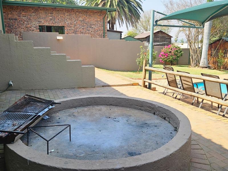 Outdoor entertainment area featuring a paved patio, built-in fire pit, and swimming pool with a shade sail.