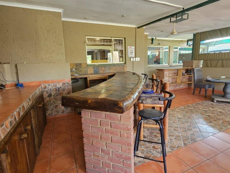 Covered outdoor patio area featuring a built-in brick bar with tiled countertop, sink, and tiled flooring, suitable for entertainment.