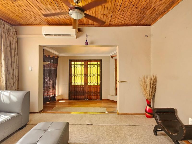 Spacious living area featuring a timber ceiling, ceiling fan, split-system air conditioning, and secure access through a metal security gate.