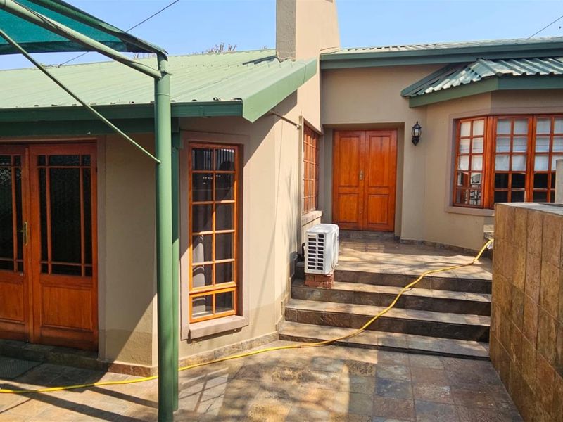 Rear exterior view of the house featuring a tiled patio area, timber framed windows and doors, and a metal roof structure.