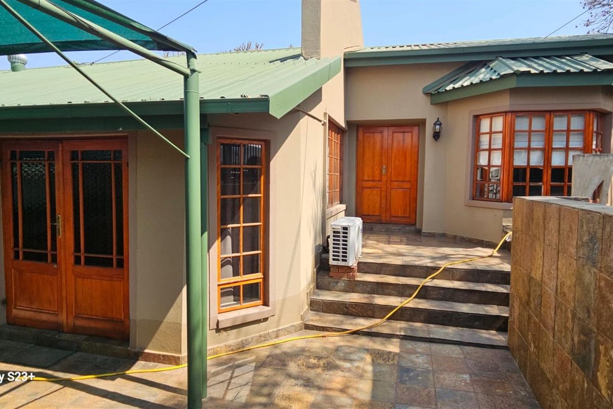 Rear exterior view of the house featuring a tiled patio area, timber framed windows and doors, and a metal roof structure.