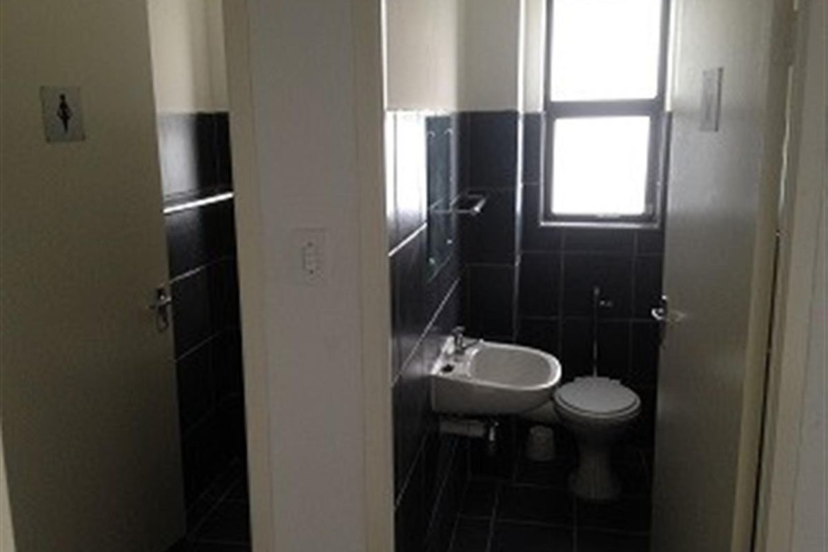 A functional industrial restroom facility featuring dark wall and floor tiling, a wall-mounted basin, and a standard toilet.