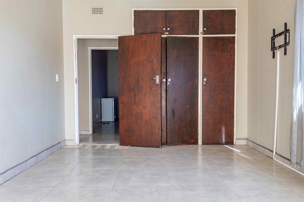 An empty bedroom featuring tiled flooring and dated built-in wooden cupboards, offering a blank canvas for renovation or interior design updates.
