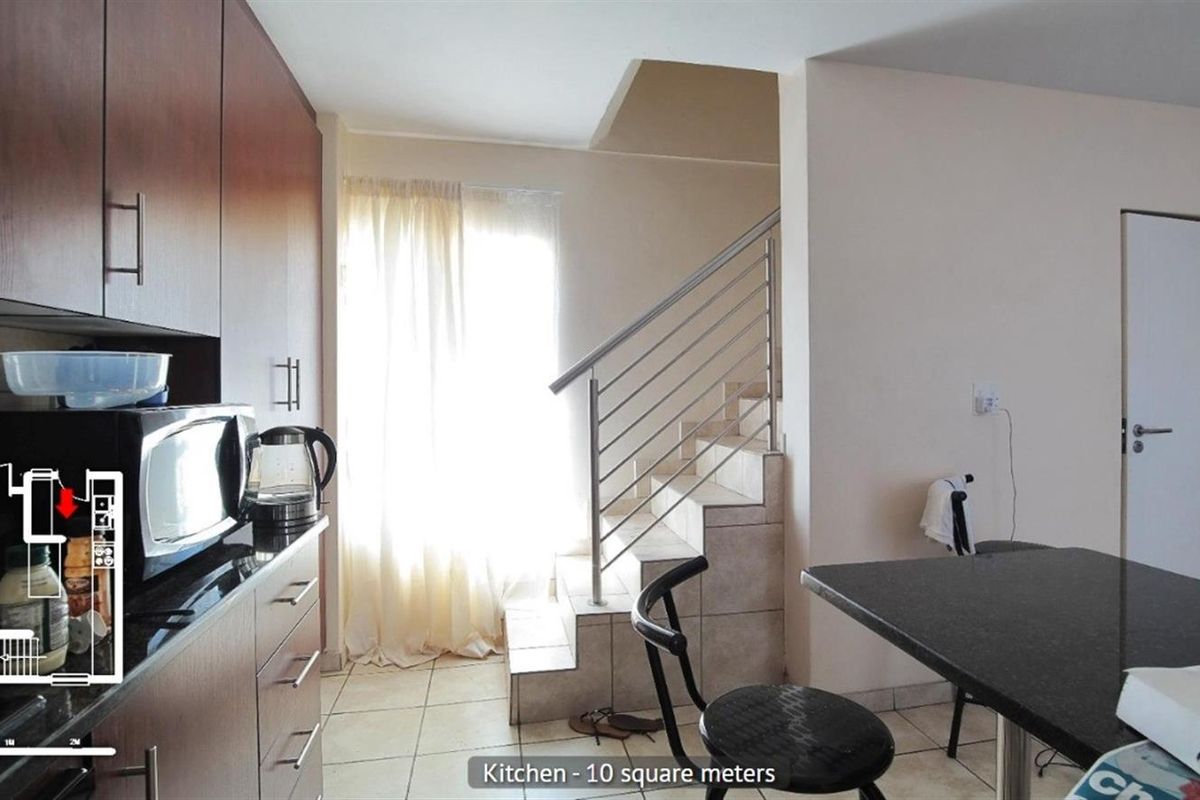 A functional kitchen area featuring dark cabinetry, granite countertops, and tiled flooring, with an adjacent staircase leading to the upper level.