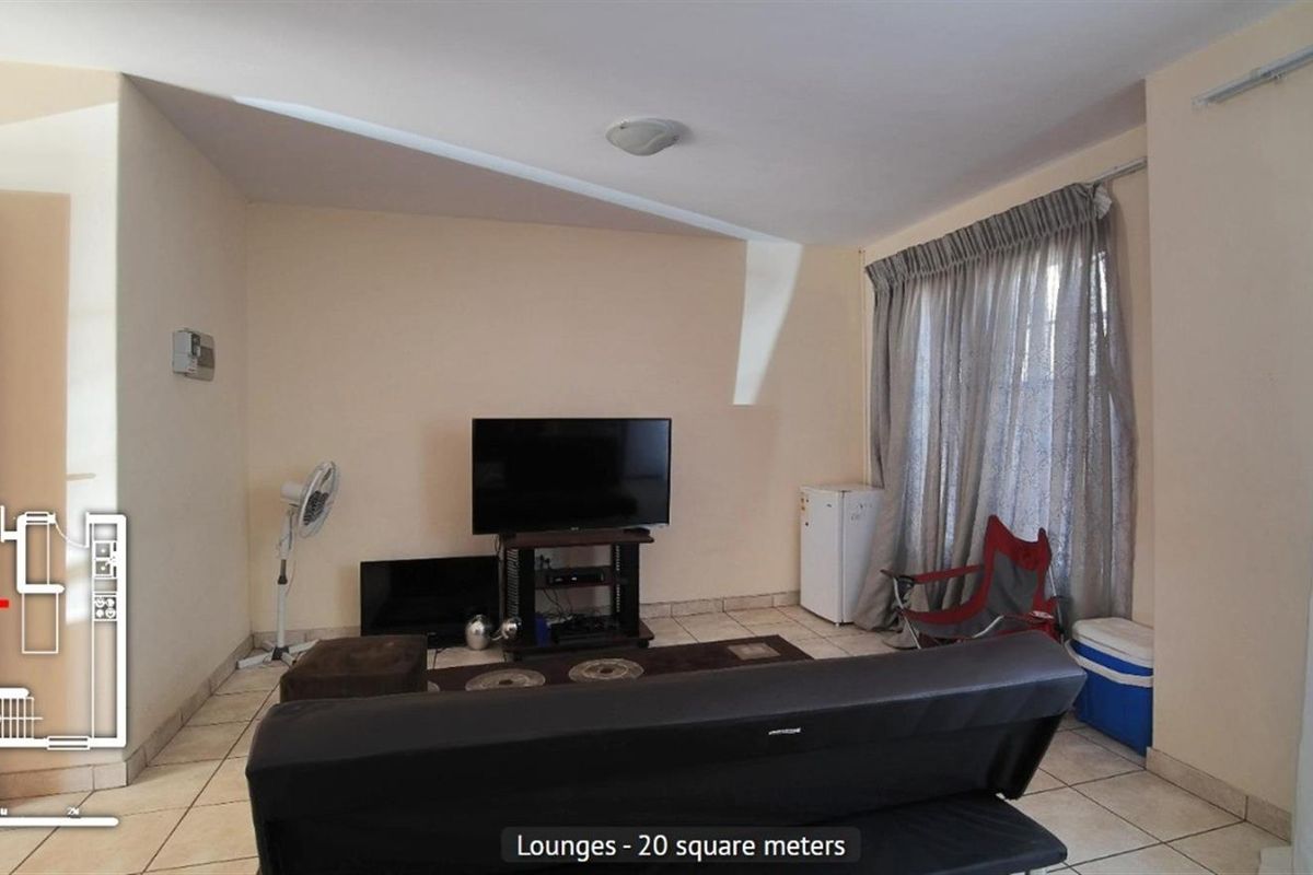 A living room area featuring tiled flooring and large windows with curtains, providing a functional space for relaxation.