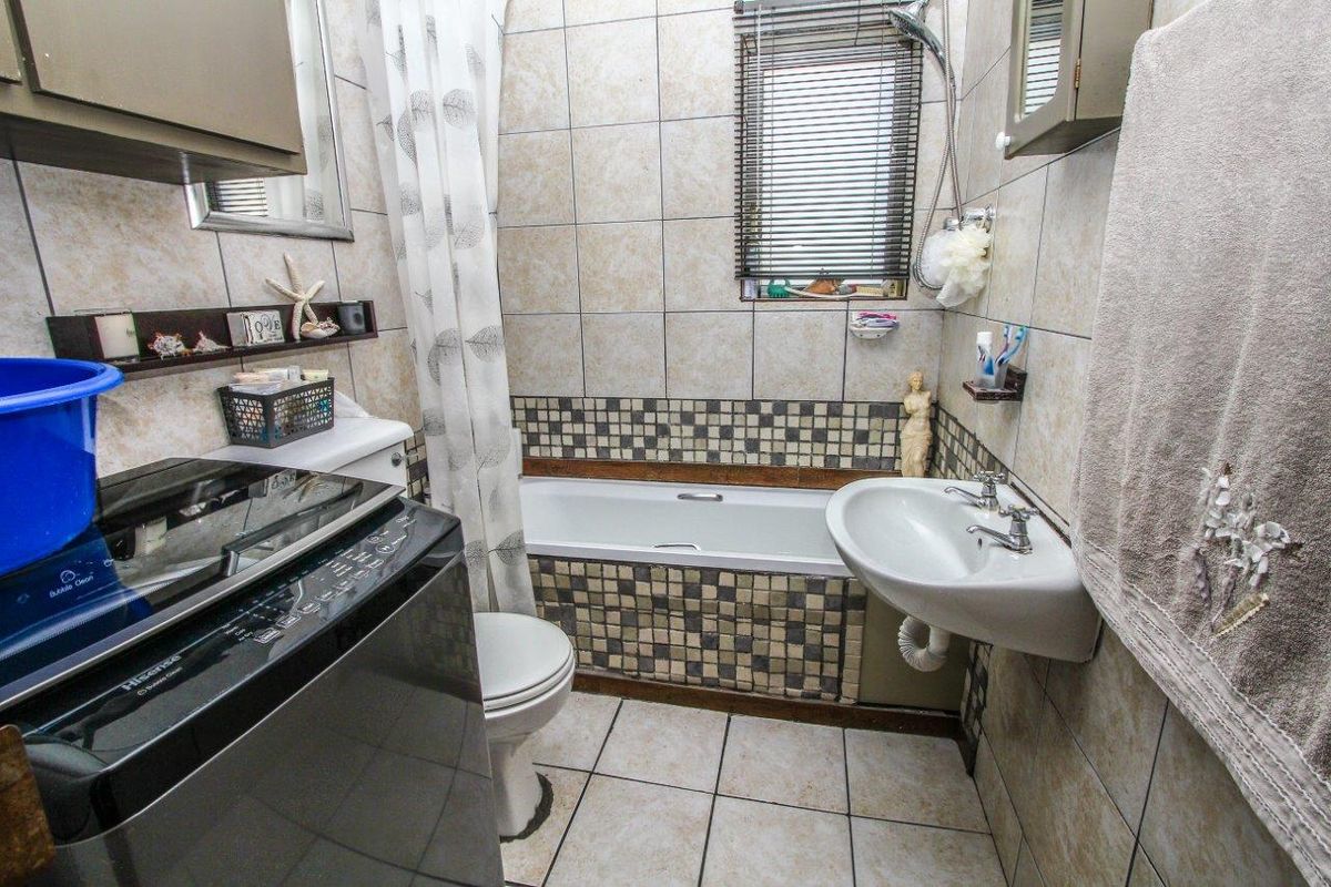 A compact bathroom featuring a bathtub with shower attachment, wall-mounted basin, and tiled finishes throughout.