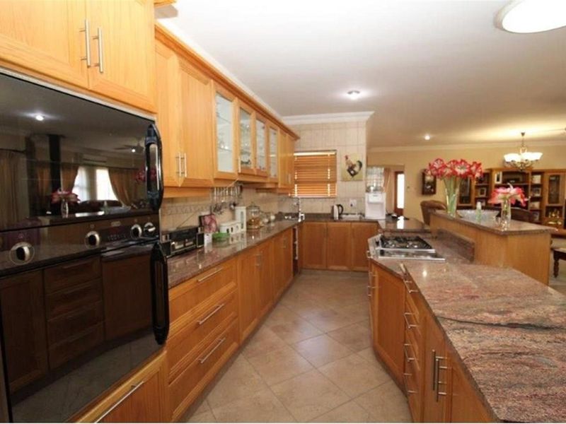 Spacious kitchen featuring timber cabinetry, granite countertops, a built-in oven, and a gas hob, seamlessly flowing into the adjacent living area.