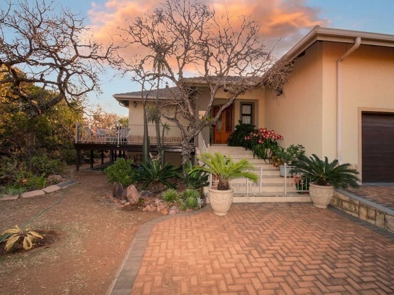 Front elevation of the house featuring a brick paved driveway, raised patio area, and integrated garage with landscaped garden surroundings.