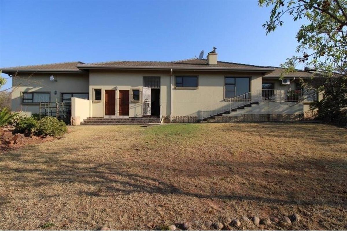 Rear view of a single-story residential house featuring a tiled roof, multiple access points, and a spacious backyard area.