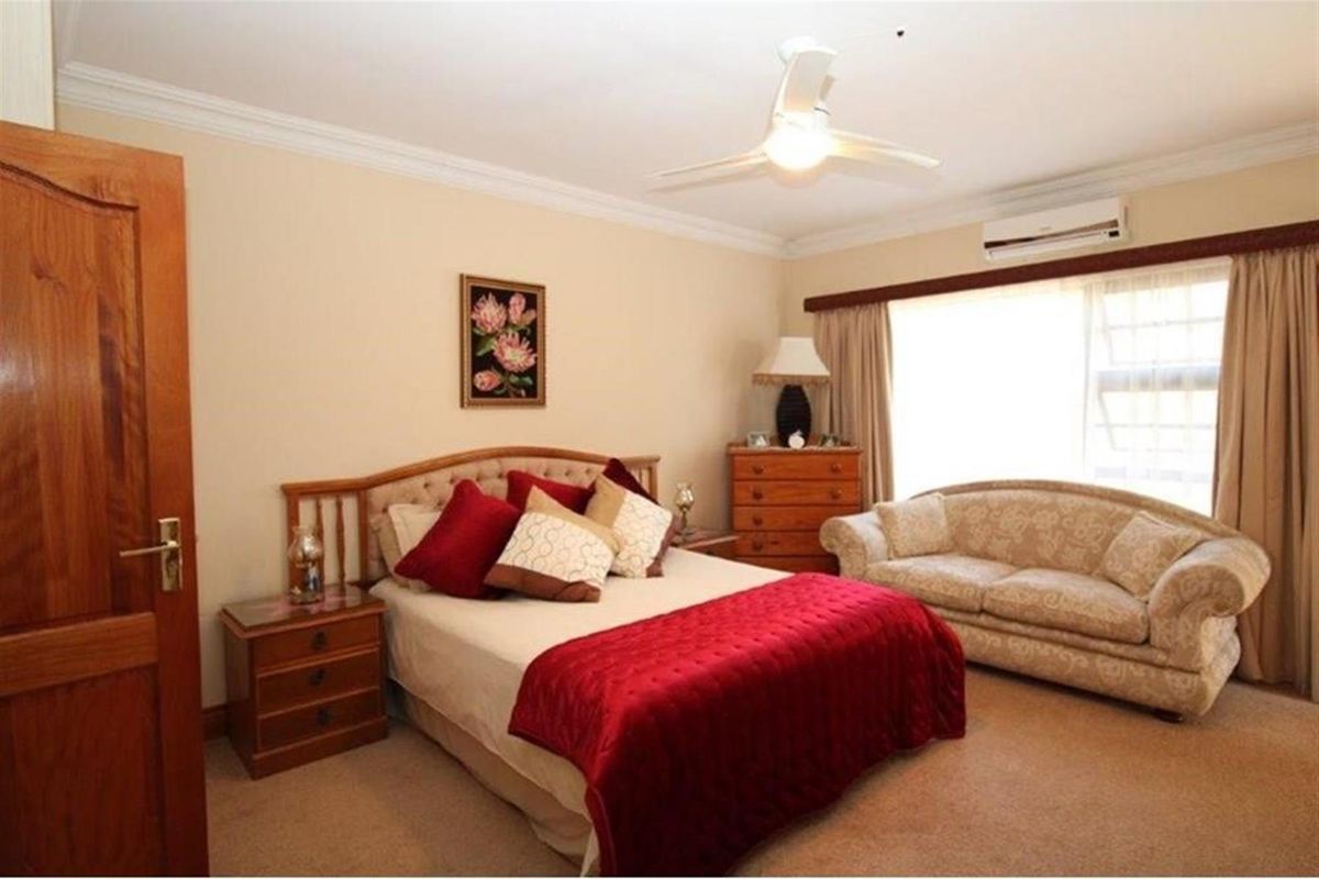 A well-maintained bedroom featuring a ceiling fan, wall-mounted air conditioning unit, and neutral carpeting.