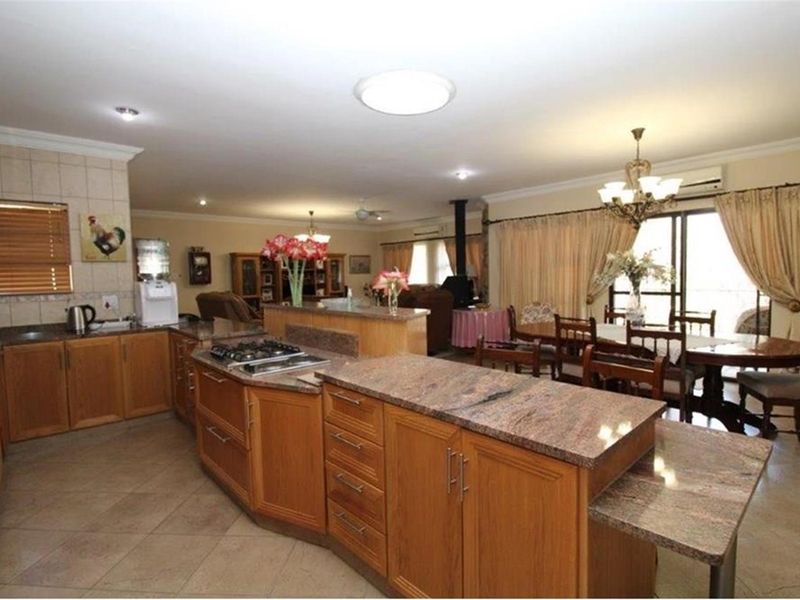 Spacious open-plan kitchen and dining area featuring wooden cabinetry, granite countertops, a built-in gas hob, and tiled flooring throughout.