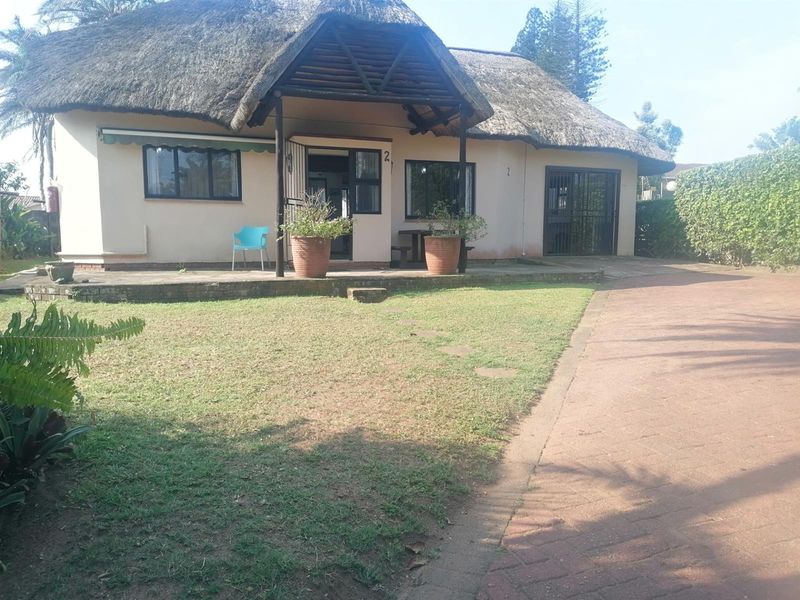 Front elevation of a townhouse featuring a traditional thatch roof, paved driveway, and a covered patio entrance area.