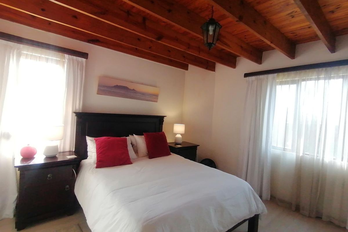 A well-lit bedroom featuring exposed timber ceiling beams and tiled flooring, creating a warm and inviting atmosphere.