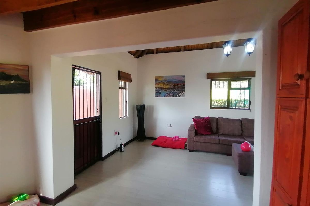 A living room featuring exposed timber ceiling beams, laminate flooring, and security features including a gate and burglar bars on the windows.