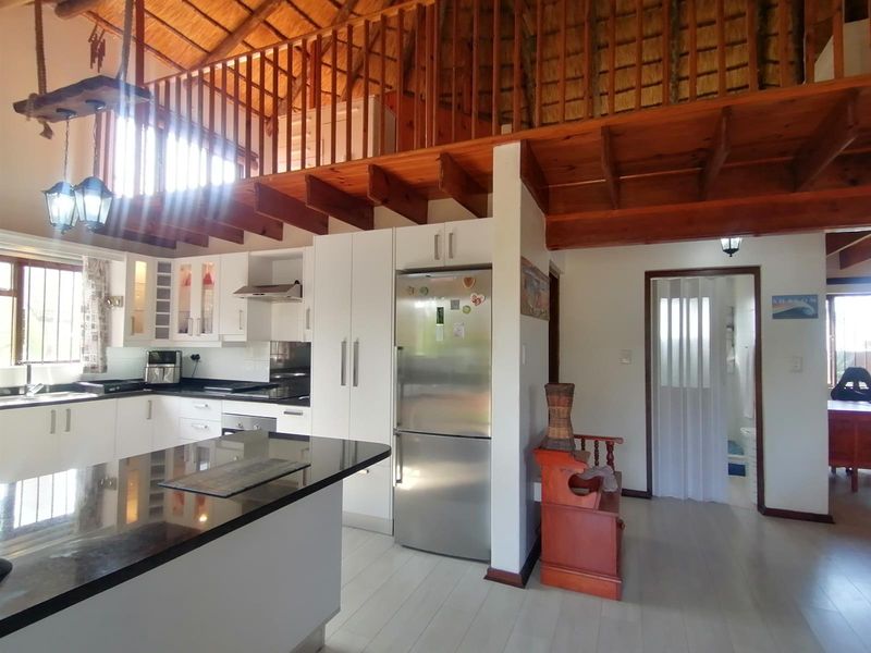 Open-plan kitchen featuring modern white cabinetry, granite countertops, and a striking exposed timber mezzanine loft above, creating a spacious and character-filled living area.