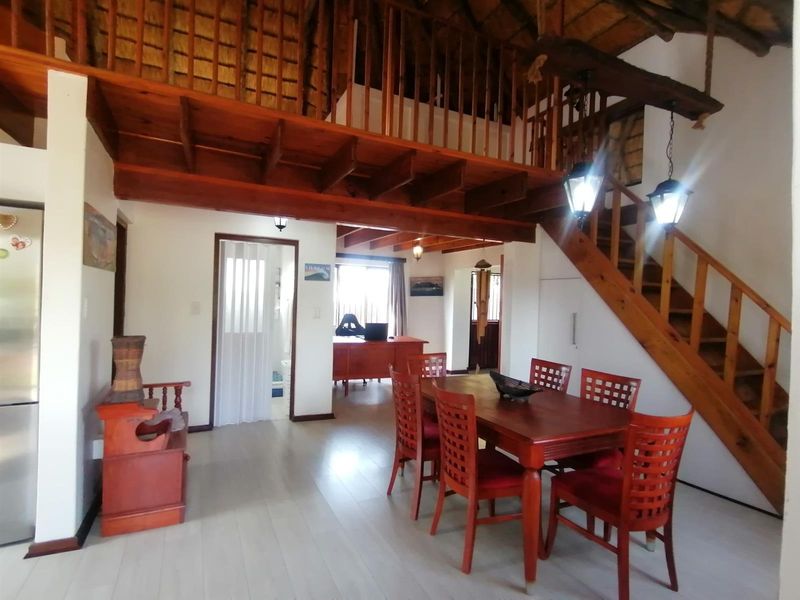 Open-plan living and dining area featuring a timber staircase, mezzanine level, exposed beams, and a traditional thatched ceiling with modern laminate flooring.