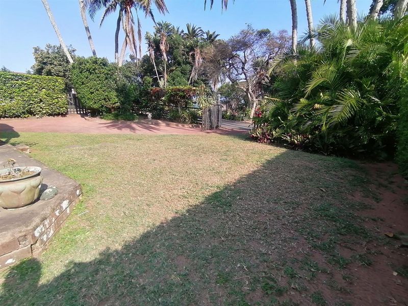 A private garden area featuring a lawn, established tropical landscaping, and a paved driveway entrance.