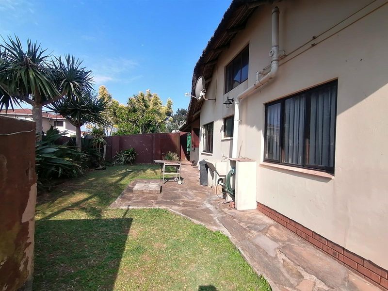 Rear exterior view of the townhouse featuring a thatched roof, stone paved walkway, and a private garden area with brick boundary walls.