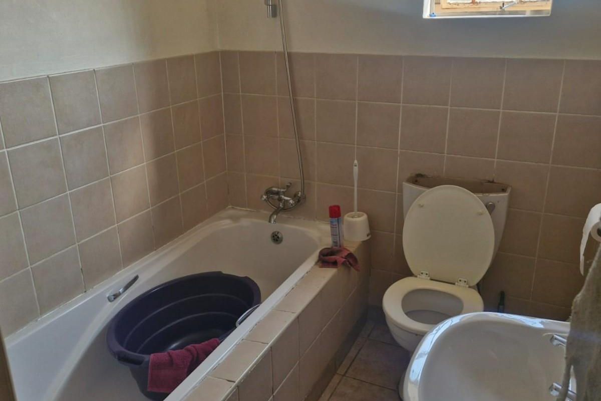 A functional bathroom featuring a tiled bathtub with shower mixer, a pedestal basin, and a toilet, requiring some cosmetic updates.