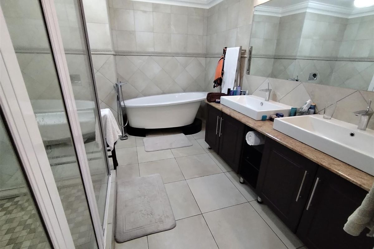 A spacious bathroom featuring a double vanity with stone countertop, a freestanding bathtub, and a separate glass-enclosed shower with tiled walls and flooring.